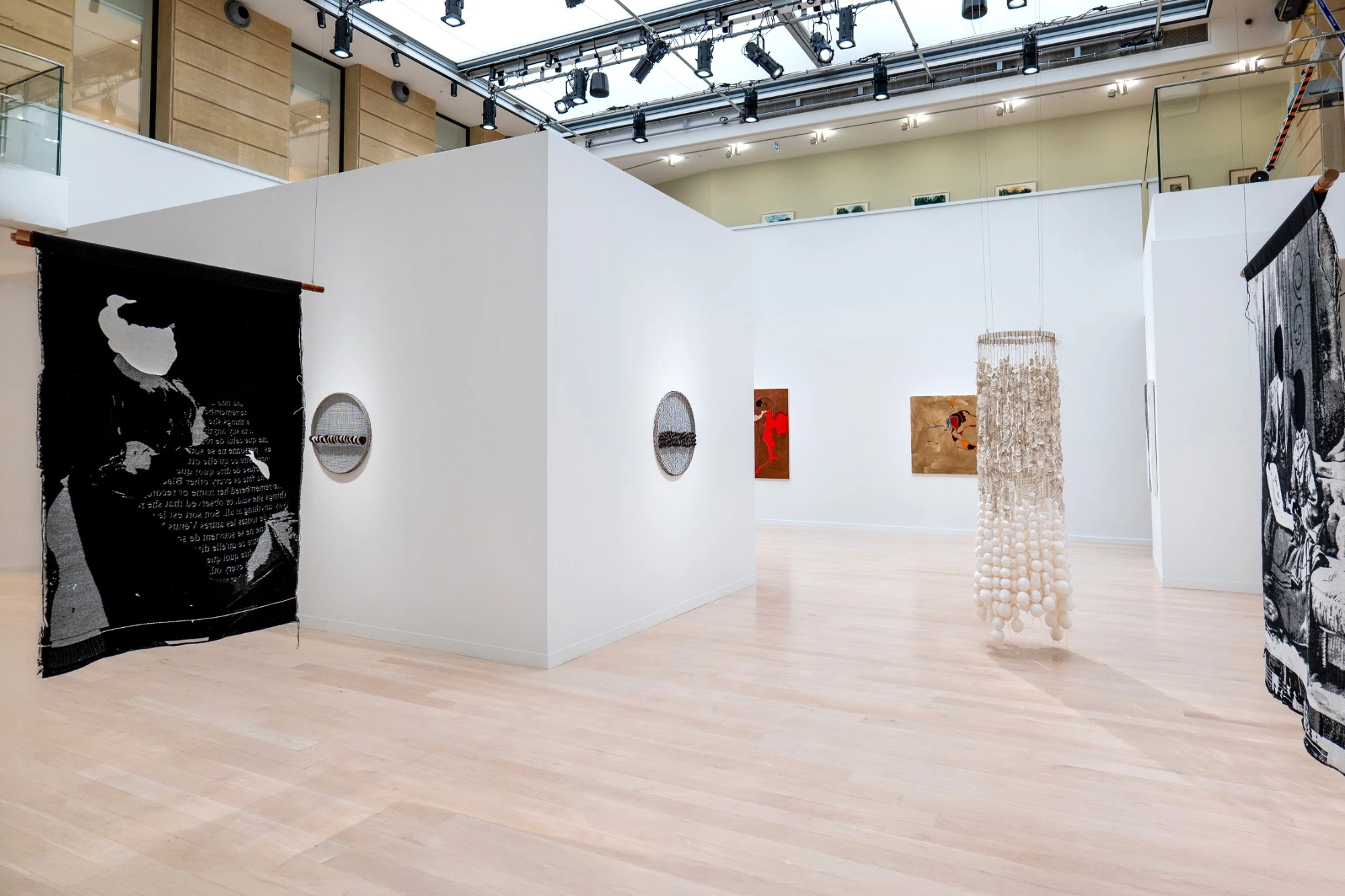 Exhibition at the Canadian Cultural Centre in Paris: free-standing white Mila-wall wall blocks under a glass roof, with hanging textile works and a sculpture in front