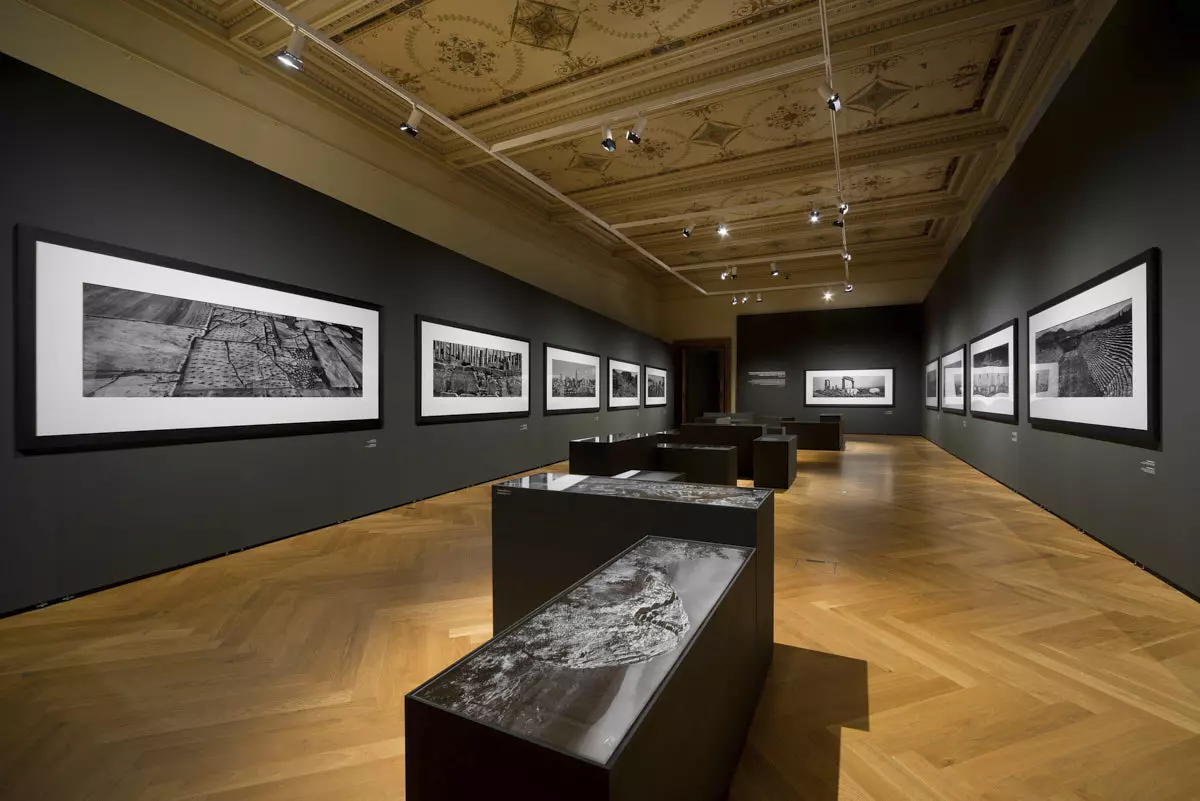 Large-format black-and-white photographs on dark Mila-wall walls at the Museum of Decorative Arts in Prague, with dark showcases in front