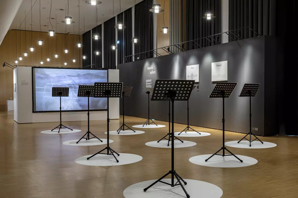 The exhibition “Musik aufs Auge” at the Württemberg State Library Stuttgart: music stands on white circles in front of a dark Mila-wall wall